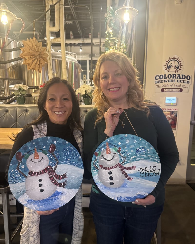 Two friends with the snowman wood-round signs they painted at a Castle Rock brewery paint night