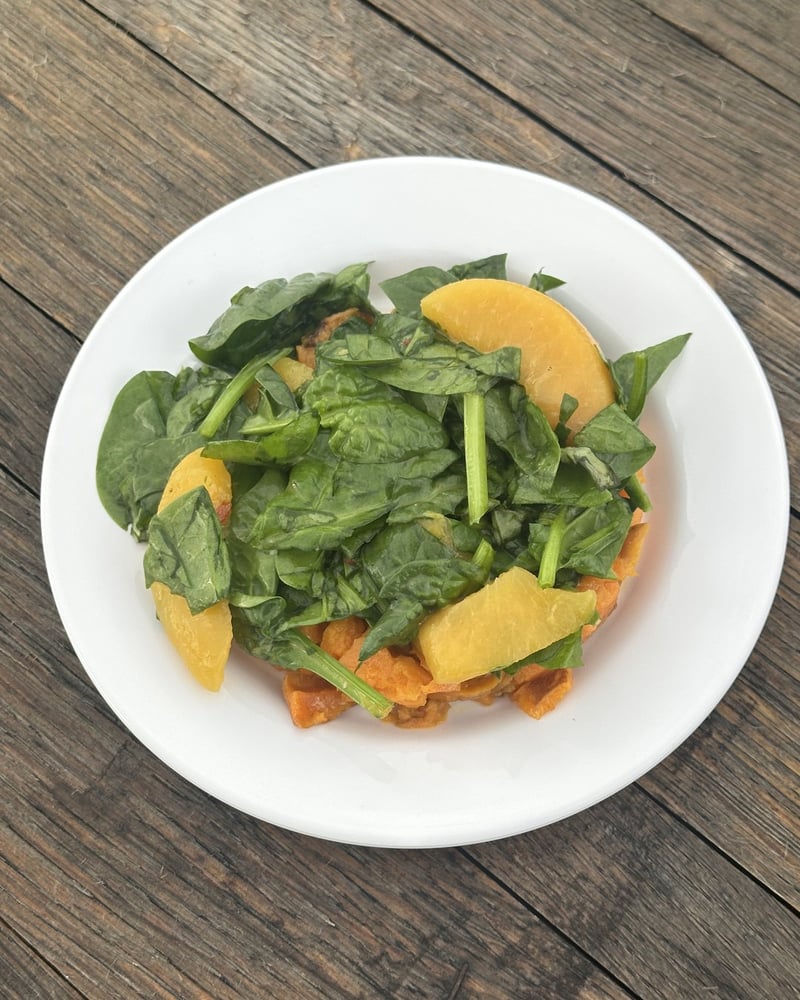A spinach and peach salad course on a wooden table