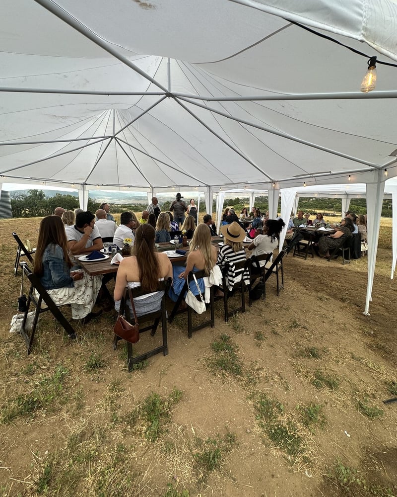 Guests at the long communal table under the tent at an outdoor supper club dinner in Douglas County