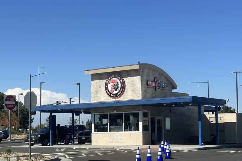 7 Brew Coffee's building and sign at Castle Pines Parkway and Debbie Lane, with the blue drive-thru awning, a car at the window and traffic cones in the lot