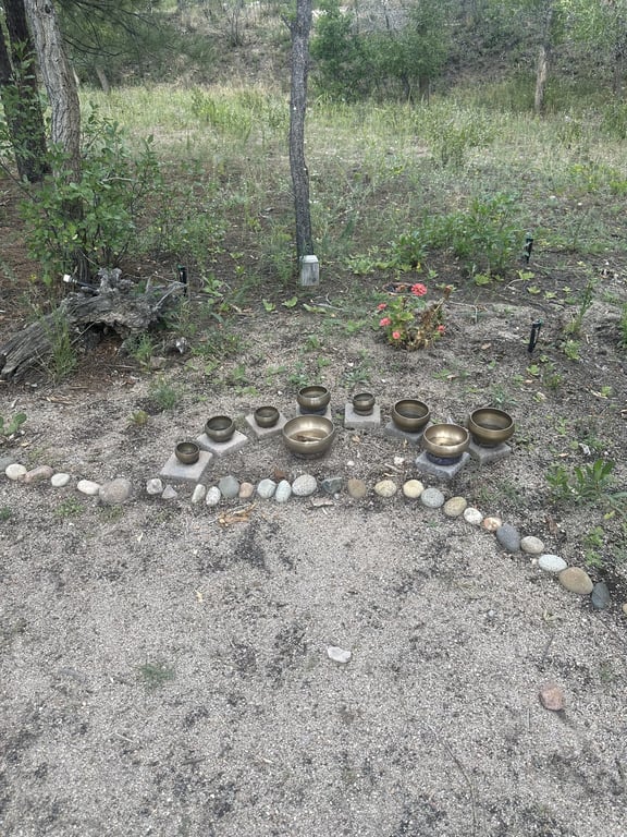 Brass singing bowls set on stone plinths along a river-rock path
