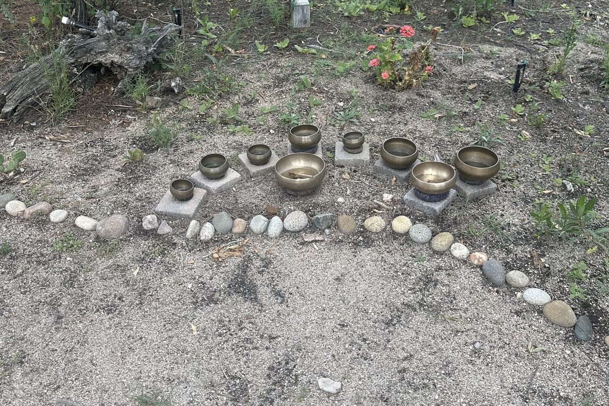 Brass singing bowls on stone plinths along a river-rock path