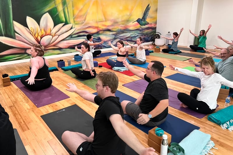 A yoga class with arms outstretched in front of a lotus-flower mural at Buka Yoga in downtown Castle Rock