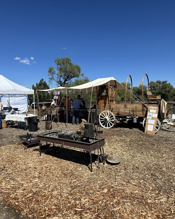 An old covered chuckwagon and a fire pit set up under a canvas awning at CALF's Harvest Day