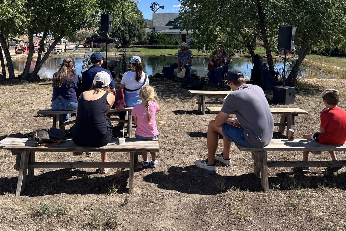 People on picnic benches listening to live music by the pond at CALF's Harvest Day