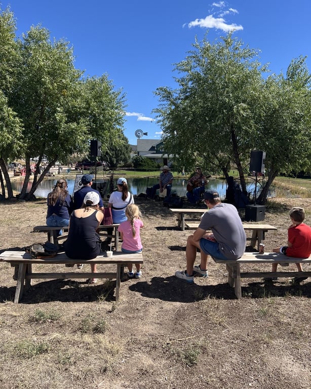 People on picnic benches listening to live music under the trees by the pond at CALF's Harvest Day