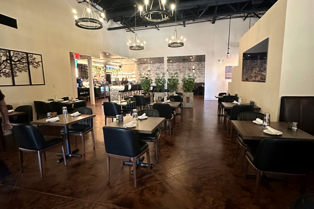 The main dining room at Castello Italiano in Castle Pines: dark chairs, wood tables and ring chandeliers under a black ceiling