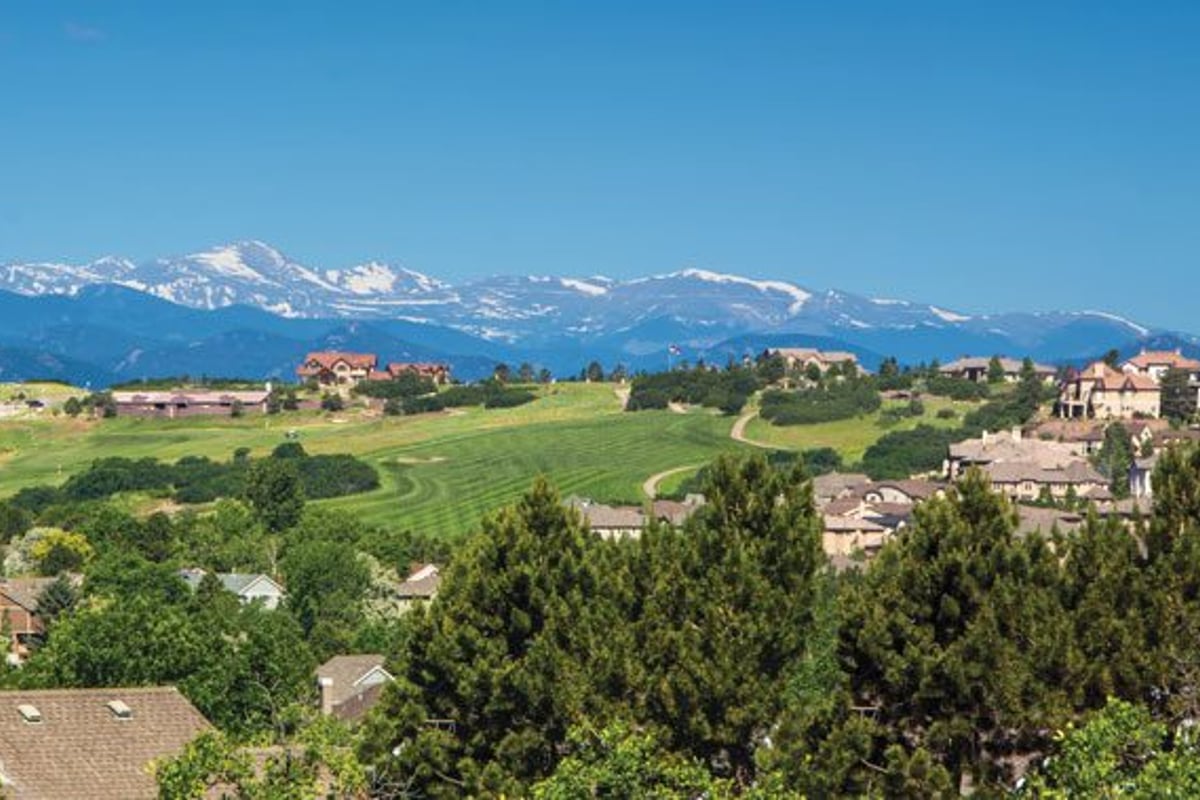 Rooftops and pines in Castle Pines with a golf fairway and the snow-capped Front Range behind