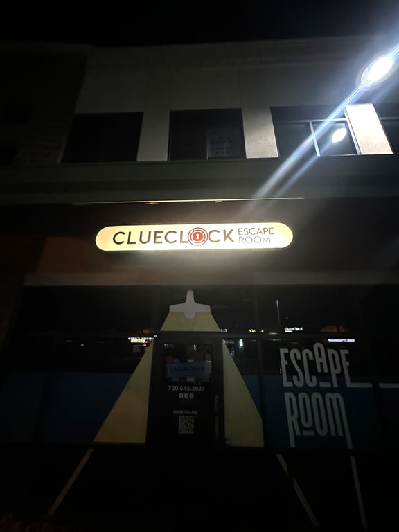 The lit ClueClock Escape Room sign on Village Square Drive at night