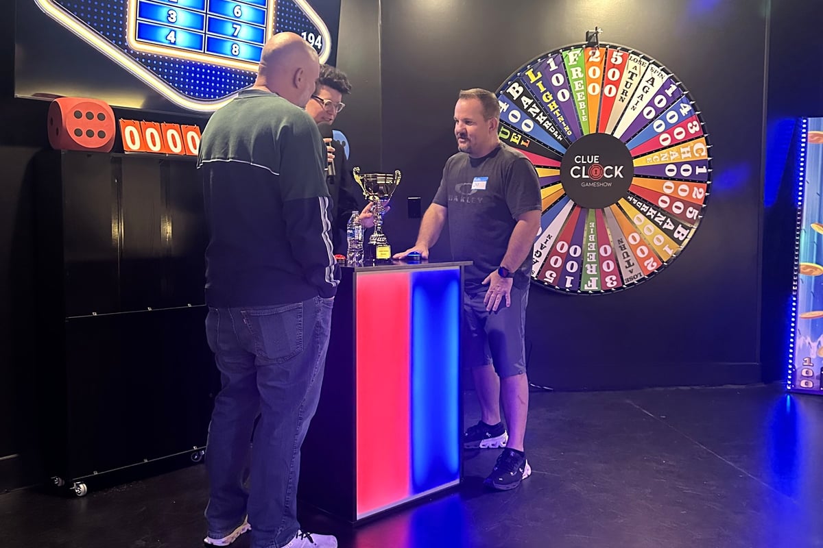 Two players face off at the buzzer podium in front of the prize wheel during Friendly Feud at the ClueClock game show in Castle Pines