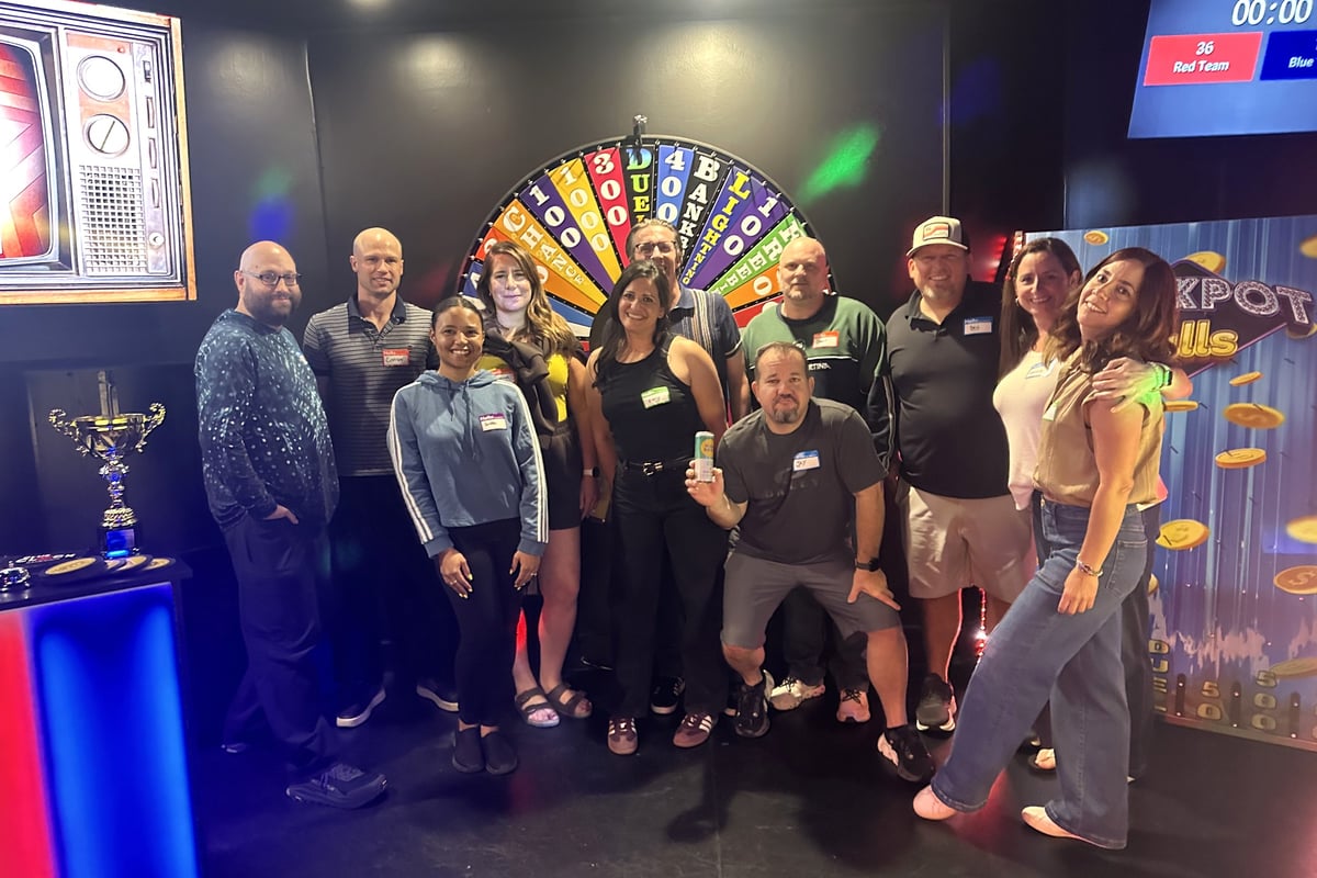 Eleven people pose in front of the prize wheel and the Jackpot Falls board after the ClueClock game show in Castle Pines