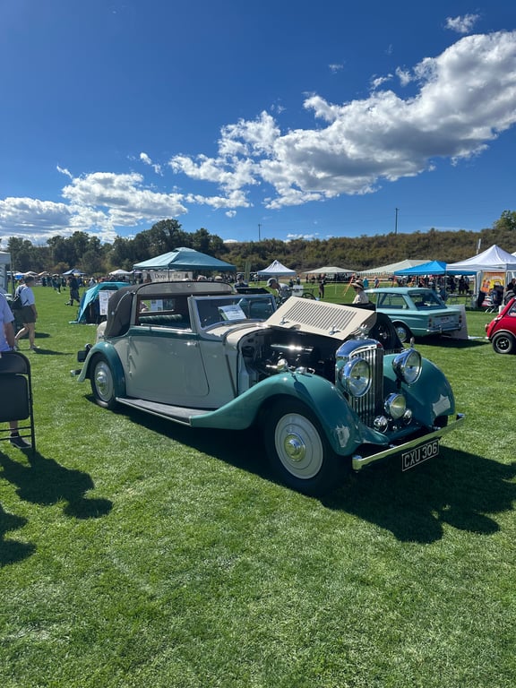 A vintage British car with a long hood on the grass at the British car show at the Colorado Highland Games