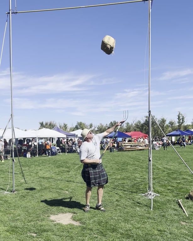 A heavy athlete in a kilt throwing a weight over the bar at the Colorado Highland Games