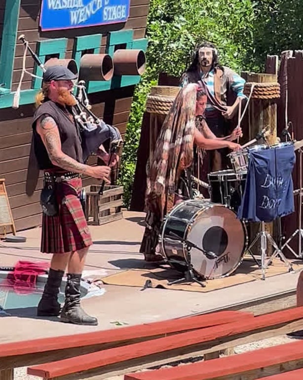 Damh & Dove, a husband-and-wife bagpipe-and-drum duo in full garb, performing on the Pirate Ship Stage at the Colorado Renaissance Festival