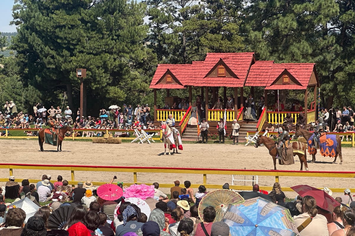 Costumed knights on horseback jousting in front of the royal viewing stand at the Colorado Renaissance Festival