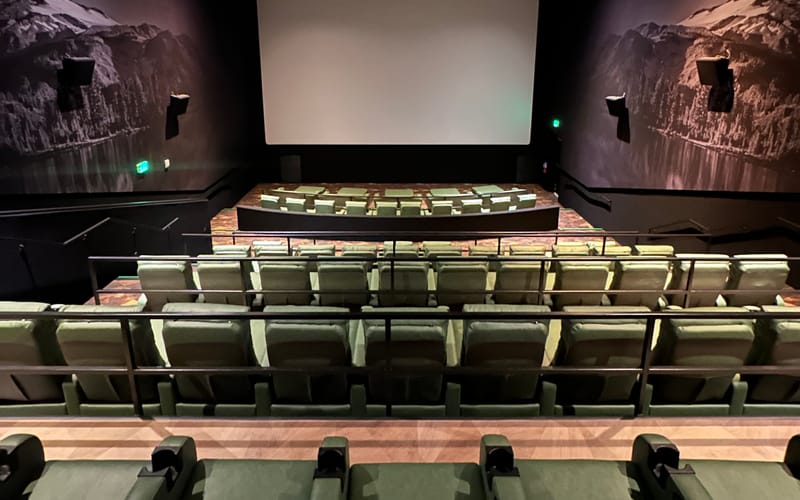 Inside an Emagine Parker auditorium, showing the big screen, heated recliners in tiered rows, and Colorado mountain-and-lake murals on both side walls.