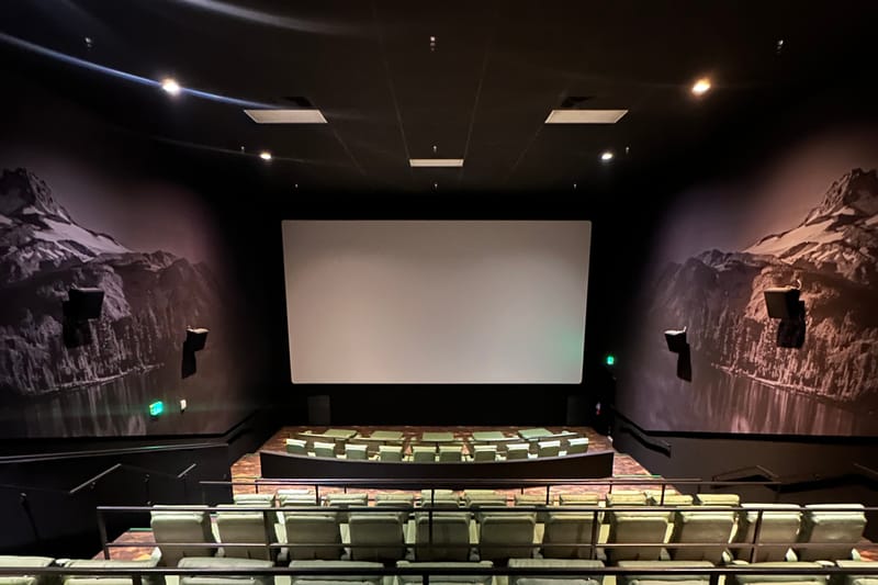 Inside an Emagine Parker auditorium, showing the big screen, heated recliners in tiered rows, and Colorado mountain-and-lake murals on both side walls.