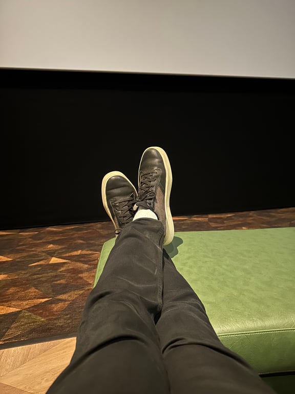 Feet up on the ottoman of a cuddle chair at Emagine Parker, a wide couch-style front-row seat facing the screen.