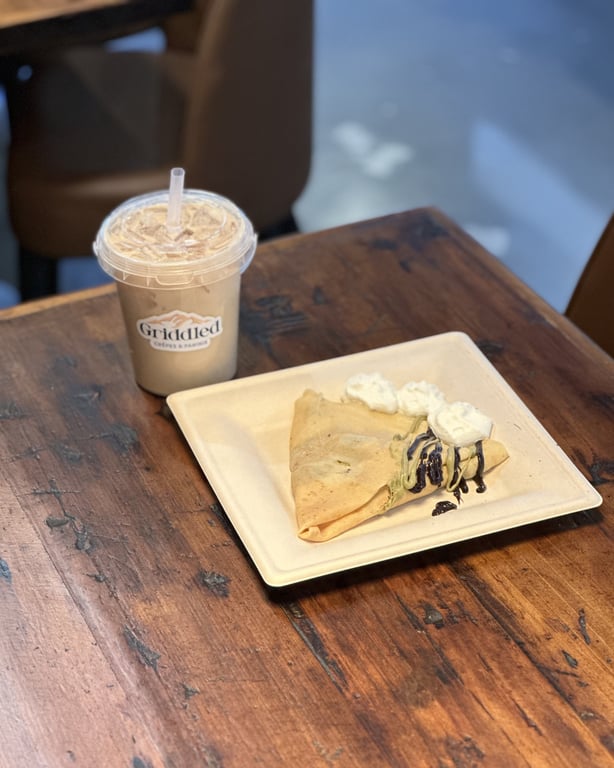 Dulce de leche iced latte in a branded Griddled cup next to a chocolate-drizzled crêpe at Griddled in Castle Rock