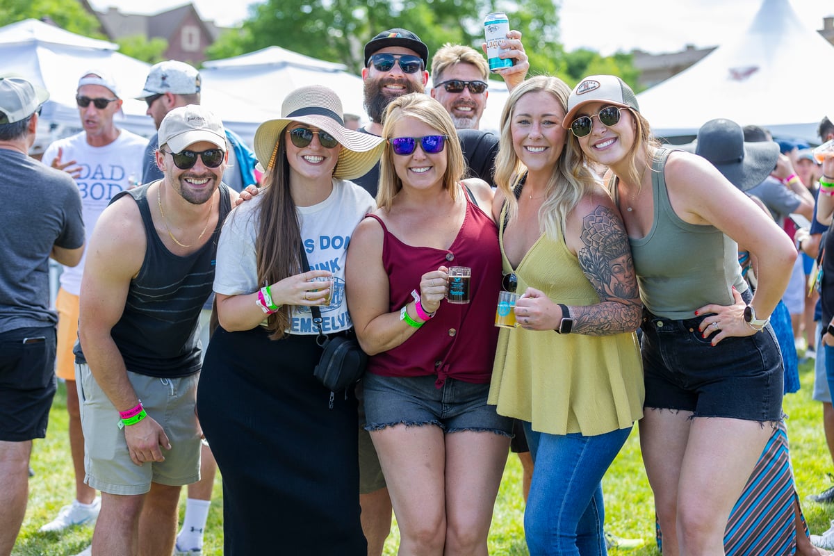 A group of friends in sunglasses and sun hats hold tasting glasses on the lawn at the Highlands Ranch Beer Festival