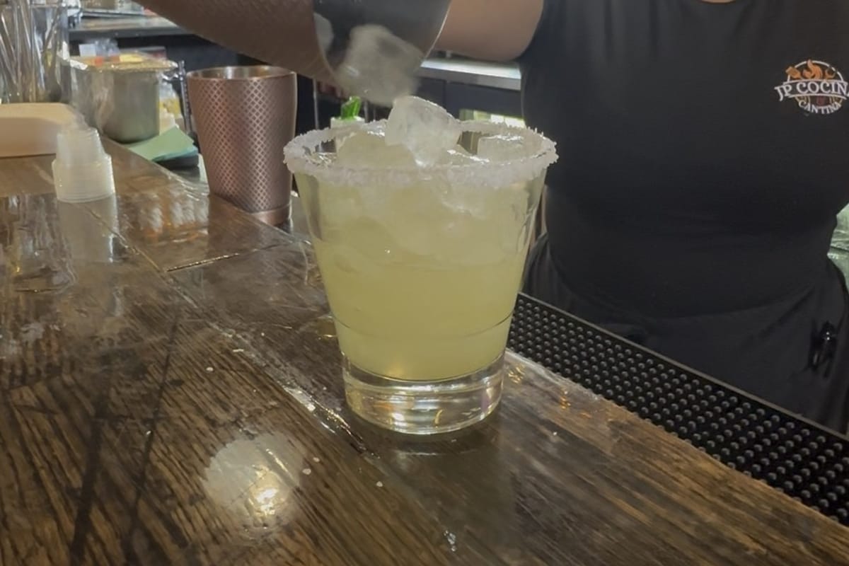 A margarita being poured from a copper shaker tin into a salt-rimmed glass