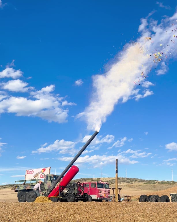 The Candy Cannon firing a plume of candy into a blue sky next to a fire truck and an army truck at Lone Creek Farms