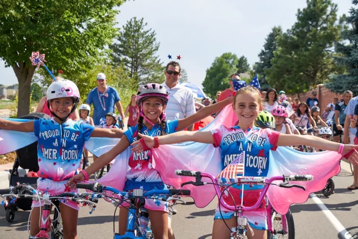 Three girls in matching red, white and blue capes ride decorated bikes in the Lone Tree Independence Day bike parade