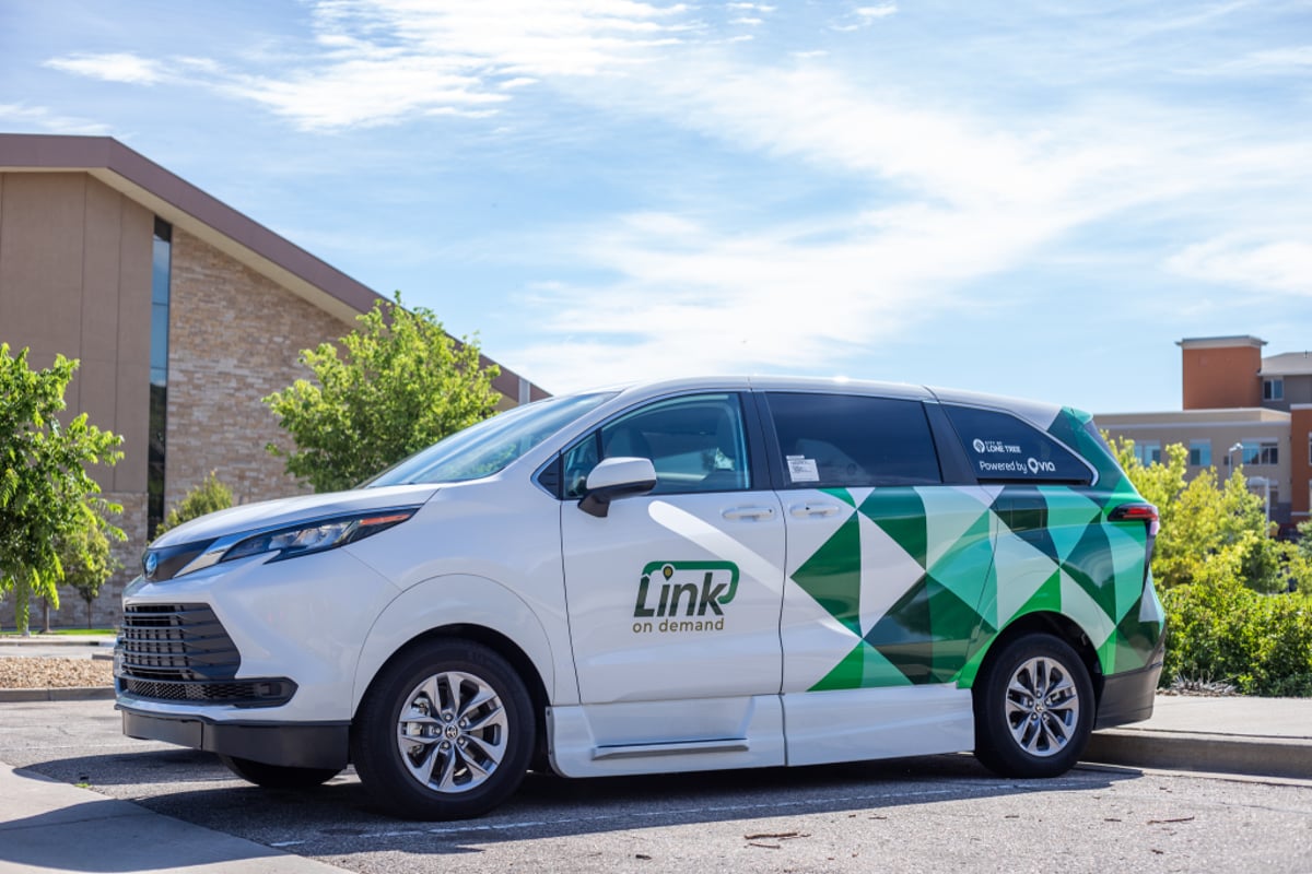 A white and green Link On Demand minivan parked outside a stone-and-glass building in Lone Tree