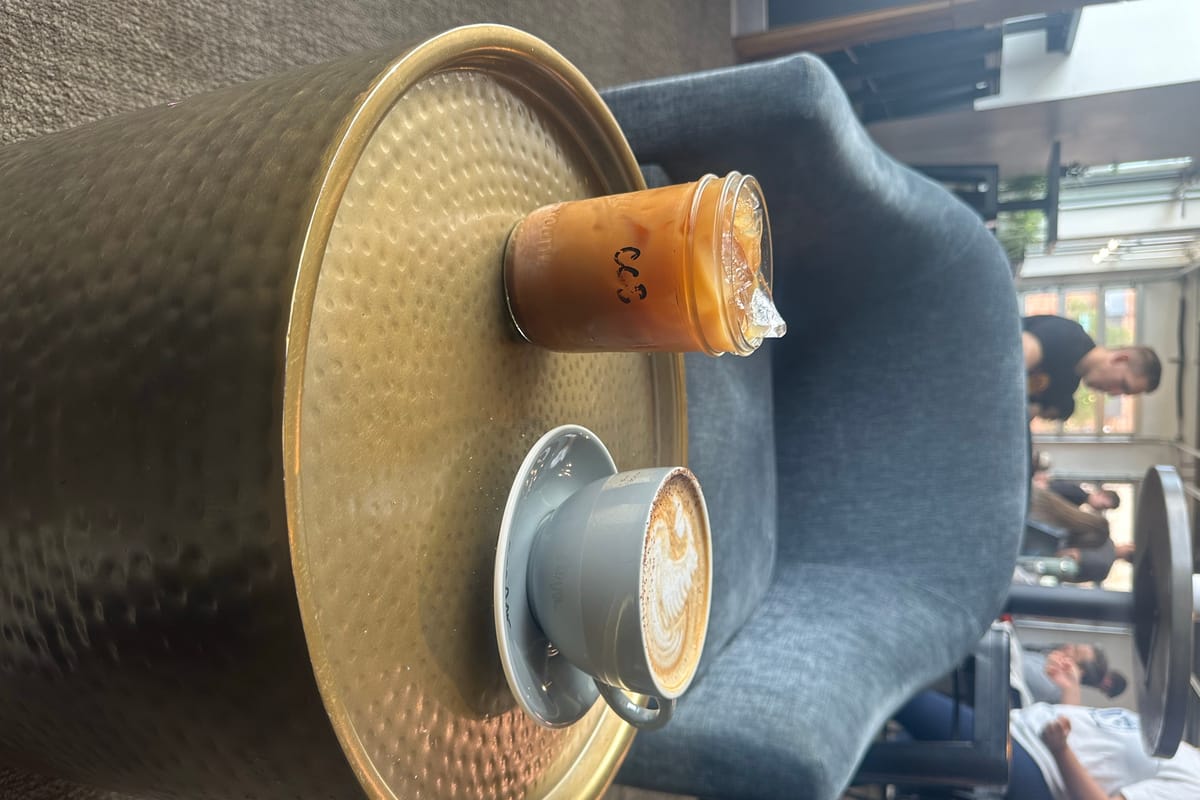 A latte with swan latte art next to an iced coffee on a round brass table at Monk & Mongoose RidgeGate