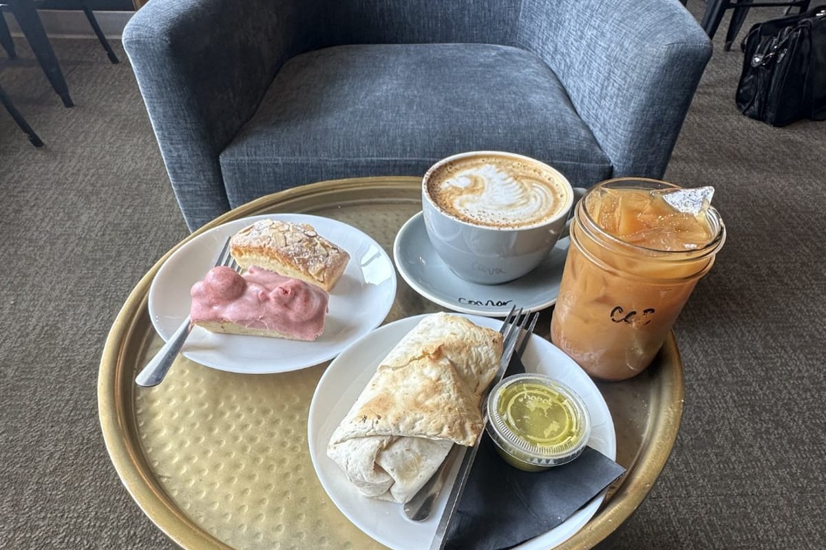Coffee, latte art, pastries, and a breakfast burrito on a table during a DougCo Social visit to Monk & Mongoose's RidgeGate location in Lone Tree