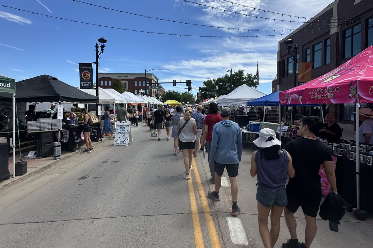 Shoppers walking down the middle of Mainstreet between vendor tents at the Parker Farmers Market