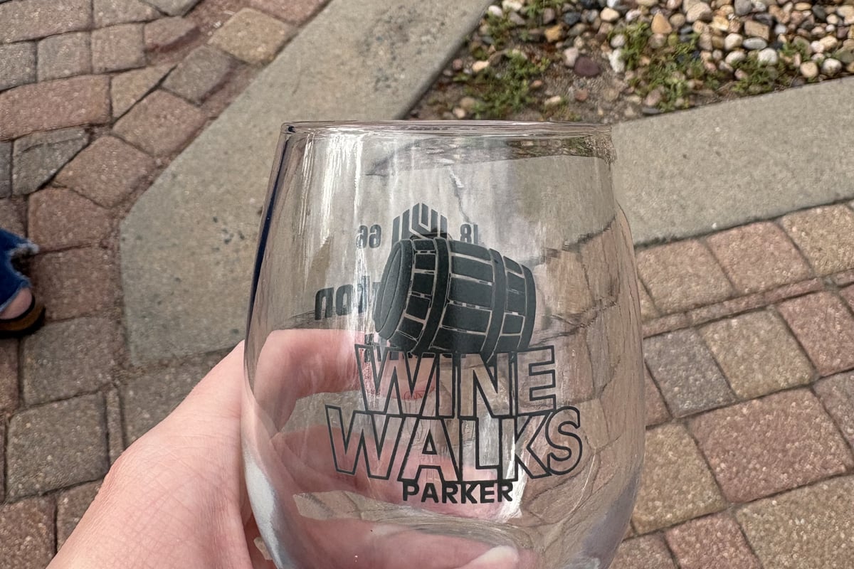 A hand holding the collectible Parker Wine Walks glass over the brick sidewalk on Mainstreet