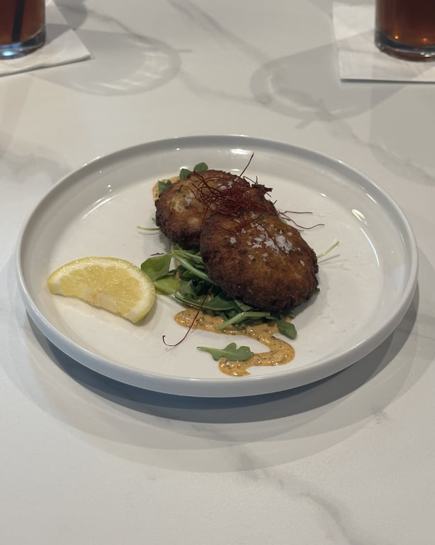 Blue Crab Cakes at Champagne Velvet Proper Kitchen & Bar — golden-brown house-made crab cakes with mustard remoulade and microgreens