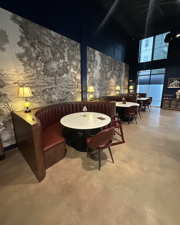 Curved booth against black-and-white landscape wallpaper at Champagne Velvet Proper Kitchen & Bar with brass lamps and marble tables