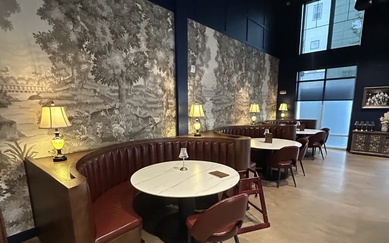 Champagne Velvet Proper Kitchen & Bar interior in Castle Rock — curved banquette against black-and-white landscape wallpaper, brass lamps, marble tables