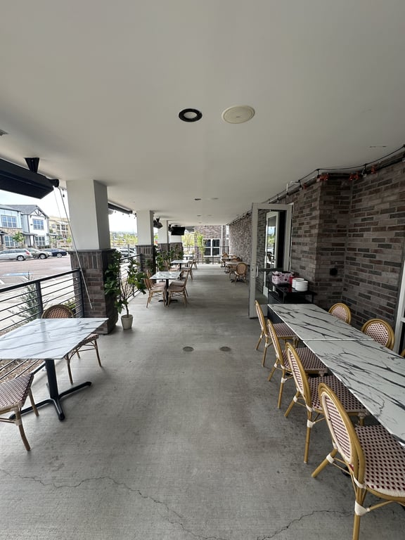 Champagne Velvet Proper Kitchen & Bar covered patio with marble bistro tables, French café chairs, brick walls, string lights