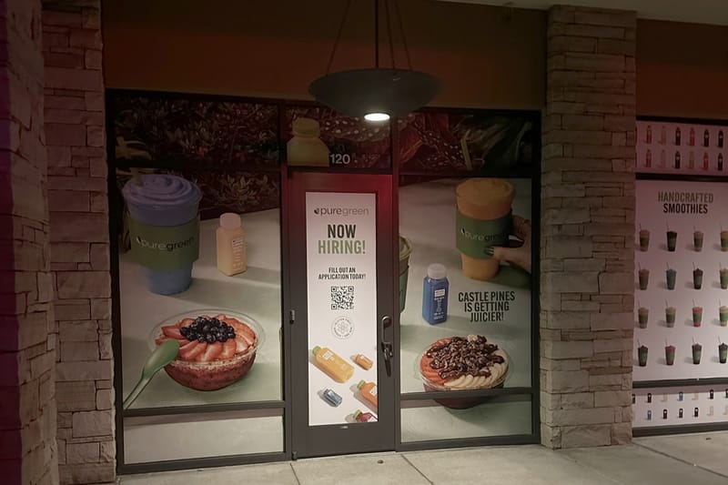Pure Green's Suite 120 storefront at the Village at Castle Pines, windows wrapped with smoothie graphics and a Now Hiring sign