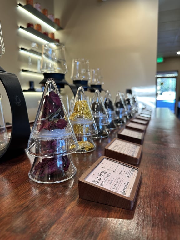 Rows of tea cones filled with dried rose and chrysanthemum along the wood tea bar at SereniTea, with tasting glasses set up above them
