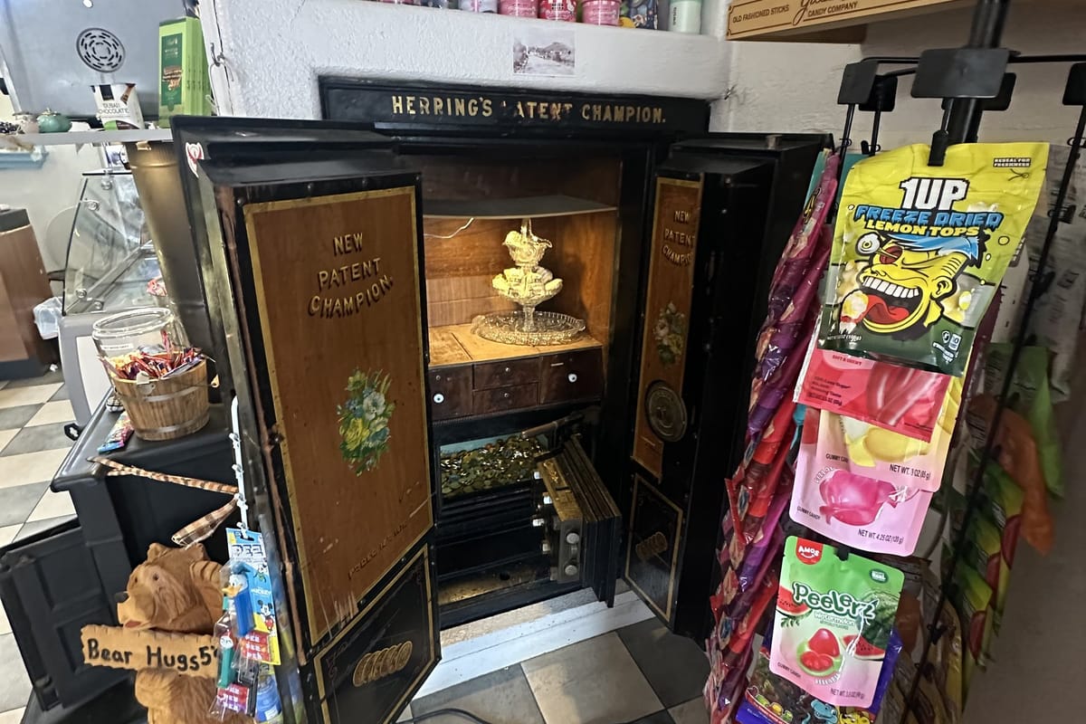 An antique Herring's Patent Champion safe standing open in the shop, beside the candy racks and a carved bear with a 'Bear Hugs 5¢' sign