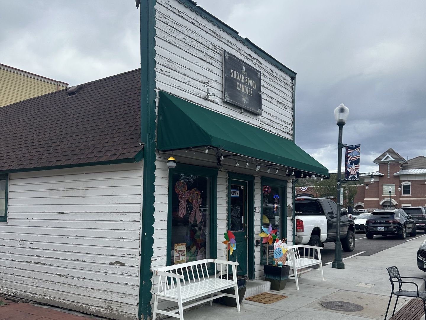 Sugar Spoon Candies at 313 Third St in downtown Castle Rock — white clapboard storefront with a green awning, hanging shop sign and two white benches out front