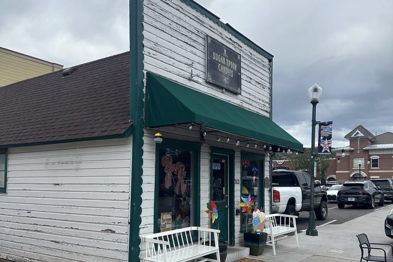 Sugar Spoon Candies at 313 Third St in downtown Castle Rock — white clapboard storefront with a green awning, hanging shop sign and two white benches out front
