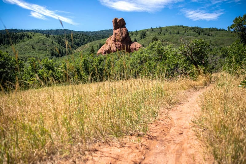 Swallowtail Trail winding through grassland below a red rock formation