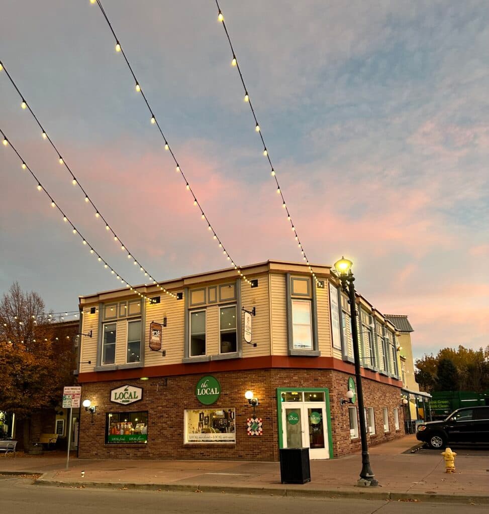 The Local at Parker storefront on Mainstreet at golden hour with festoon lights overhead, "the LOCAL market" sign visible above the corner entrance, downtown Parker, Colorado.