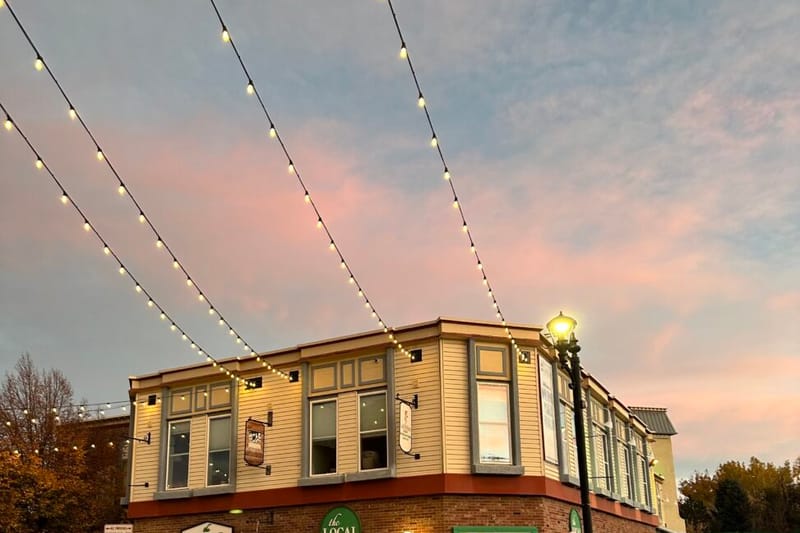 The Local at Parker storefront on Mainstreet at golden hour with festoon lights overhead, "the LOCAL market" sign visible above the corner entrance, downtown Parker, Colorado.