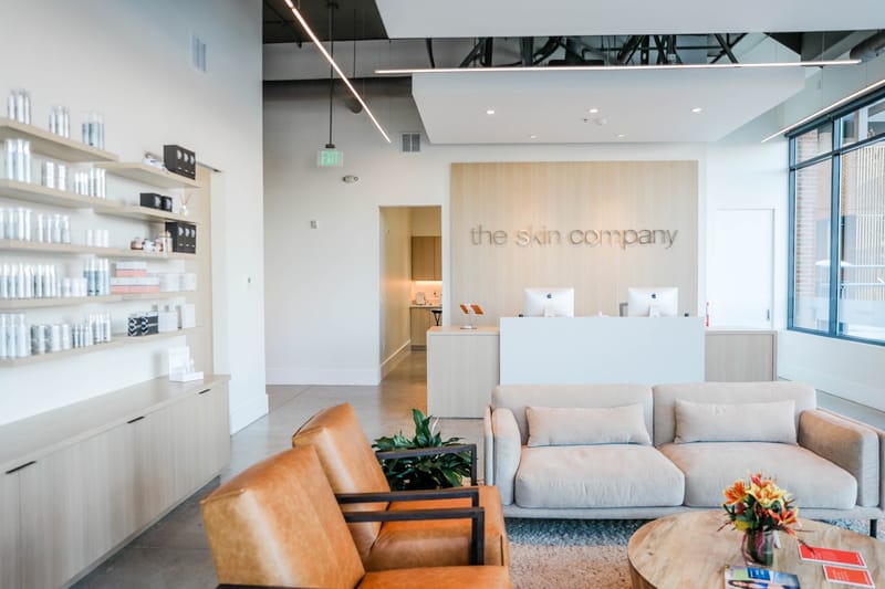 The reception area at The Skin Company in downtown Castle Rock, with the front desk, lounge seating and skincare shelves