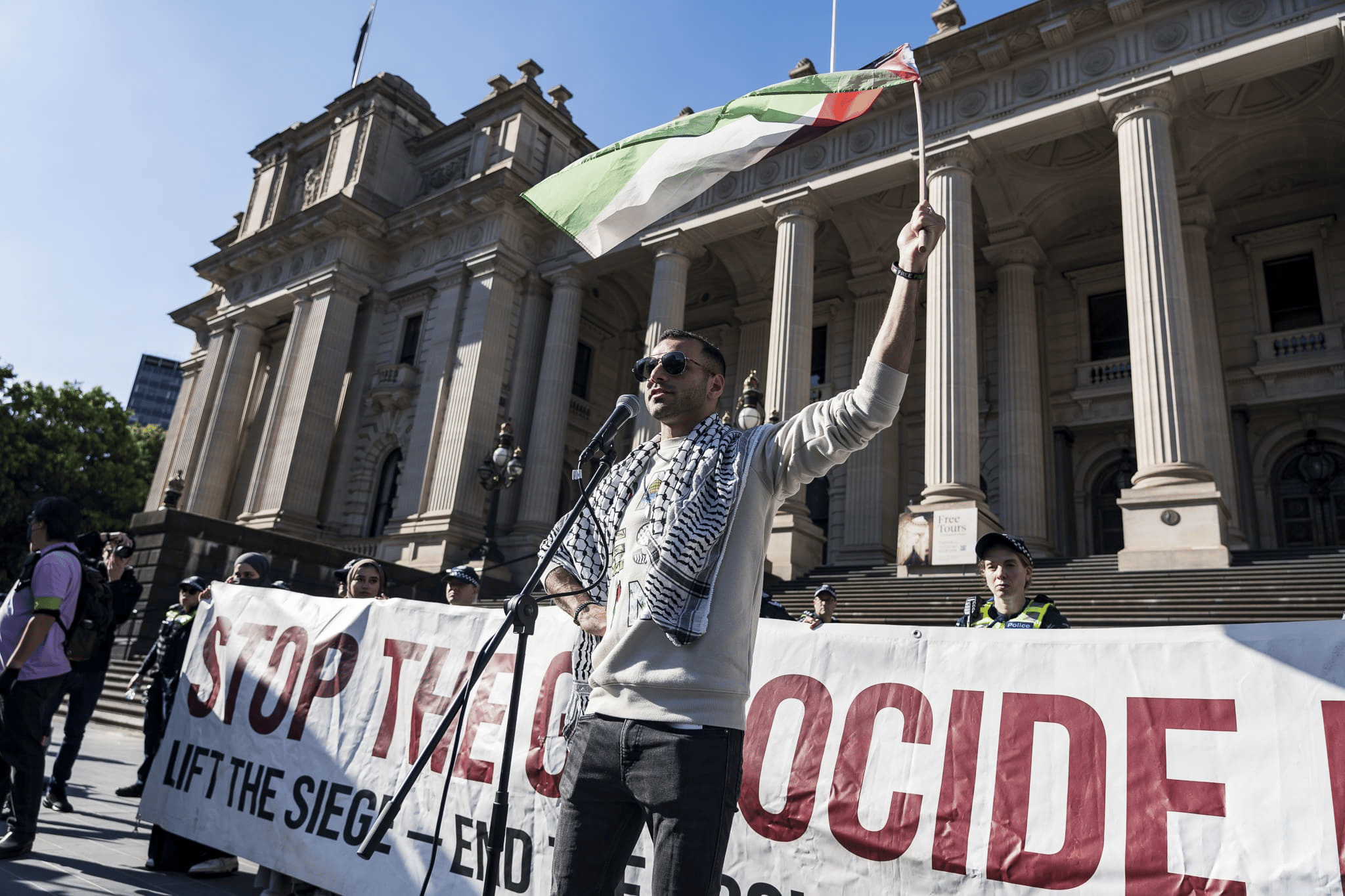 A speaker at a rally holding a Palestinian flag. Photo: Matt Hrkac