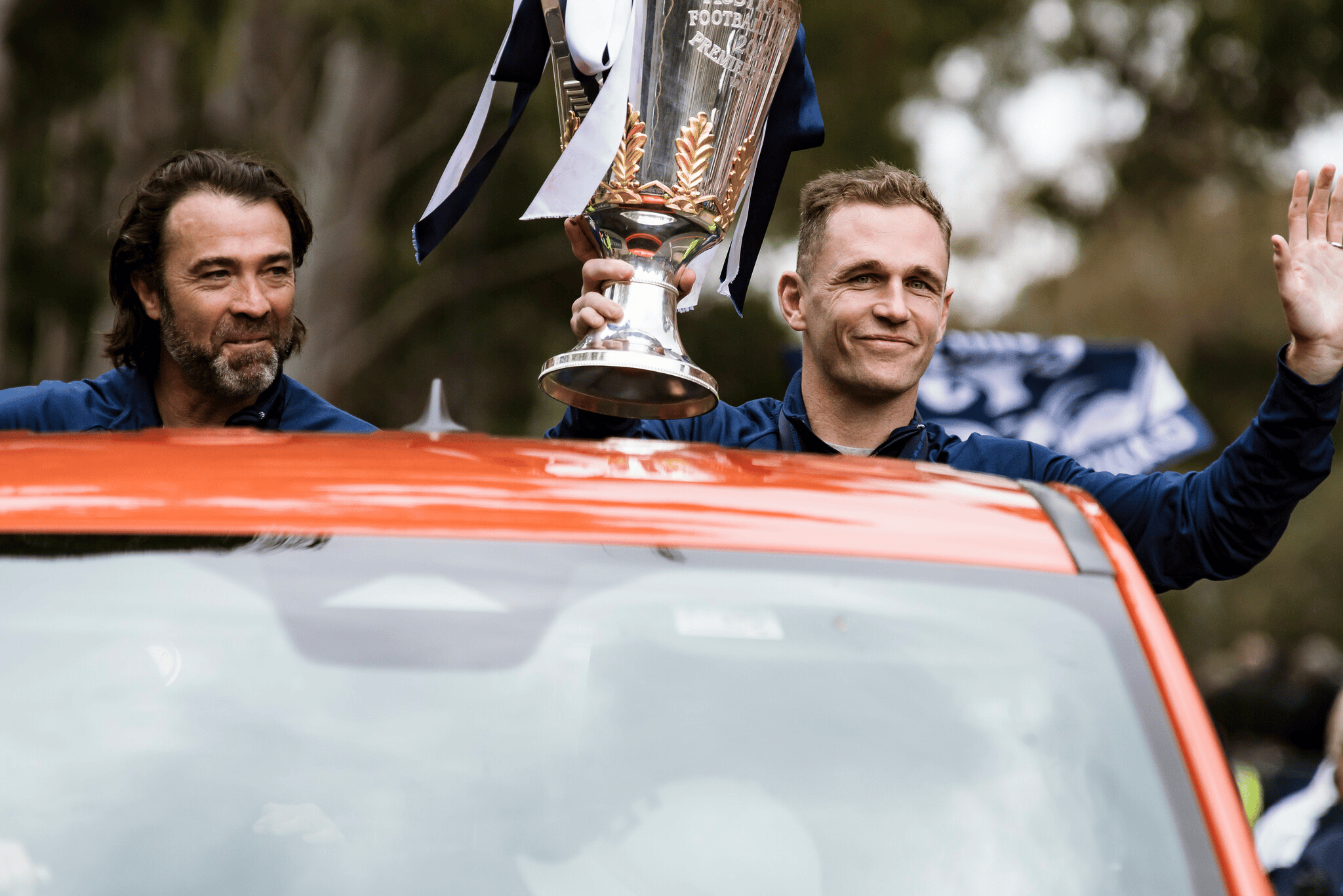 Geelong Cats coach Chris Scott sits alongside then-captain Joel Selwood who's holding the premiership cup.
