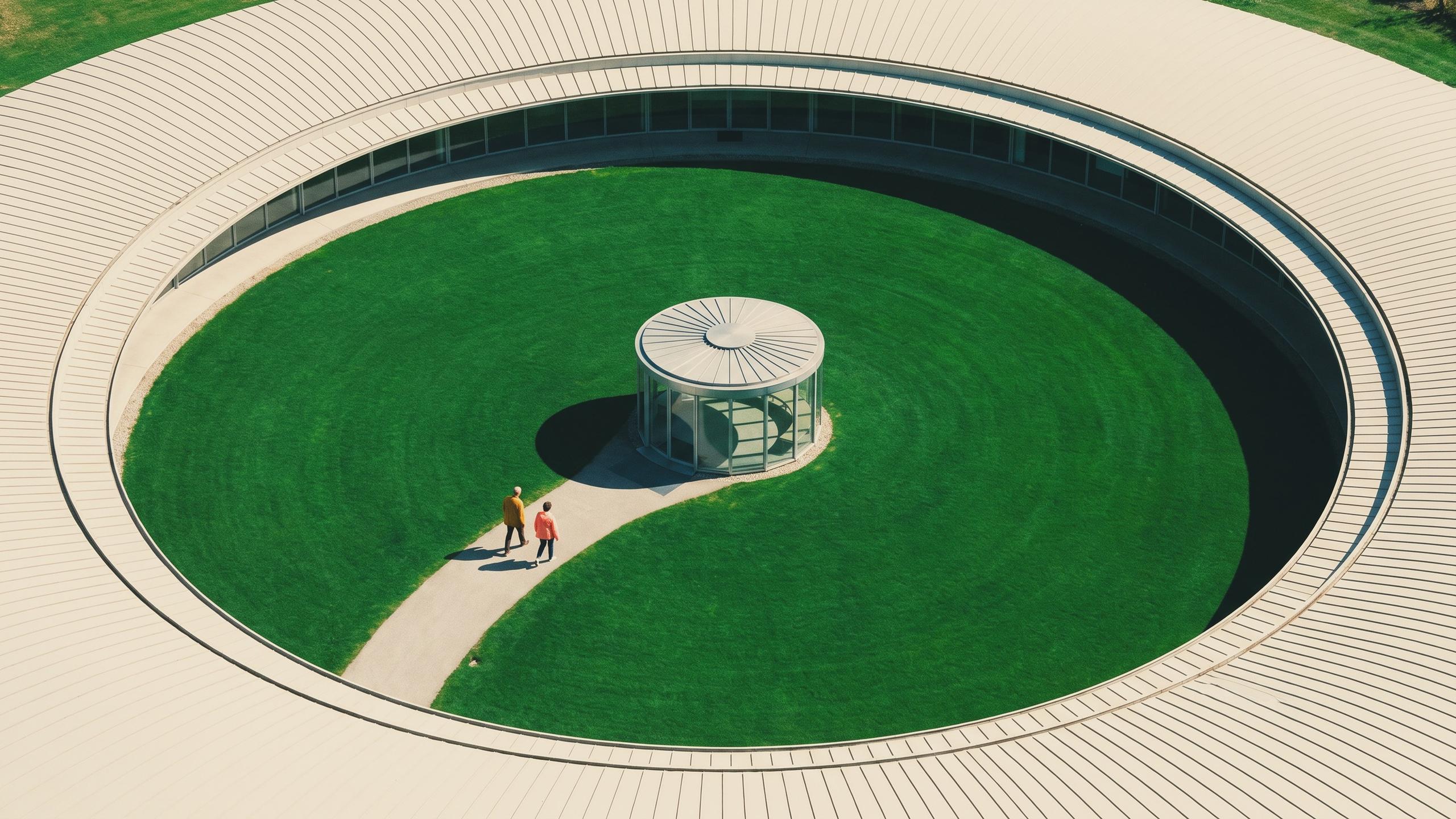 A circular building surrounding a green courtyard, with a path to a glass pavilion