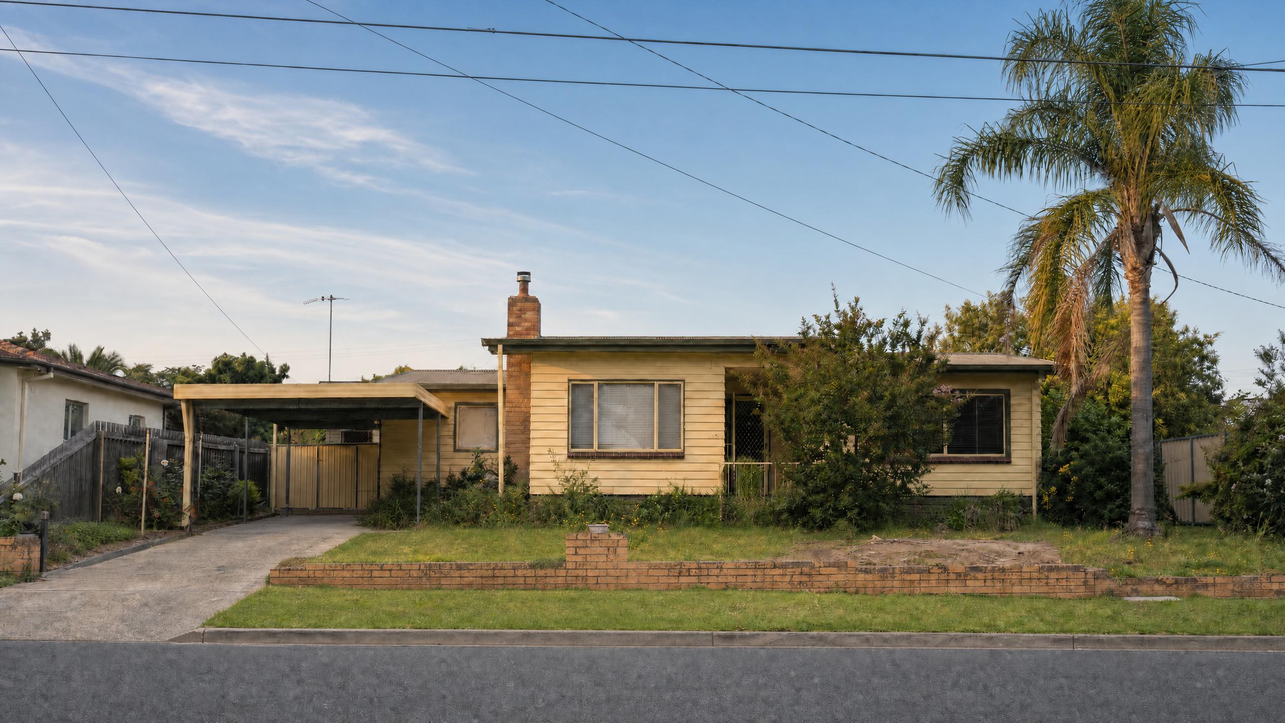A yellow weatherboard house with a carport and palm tree, edited to show a blue sky with light clouds