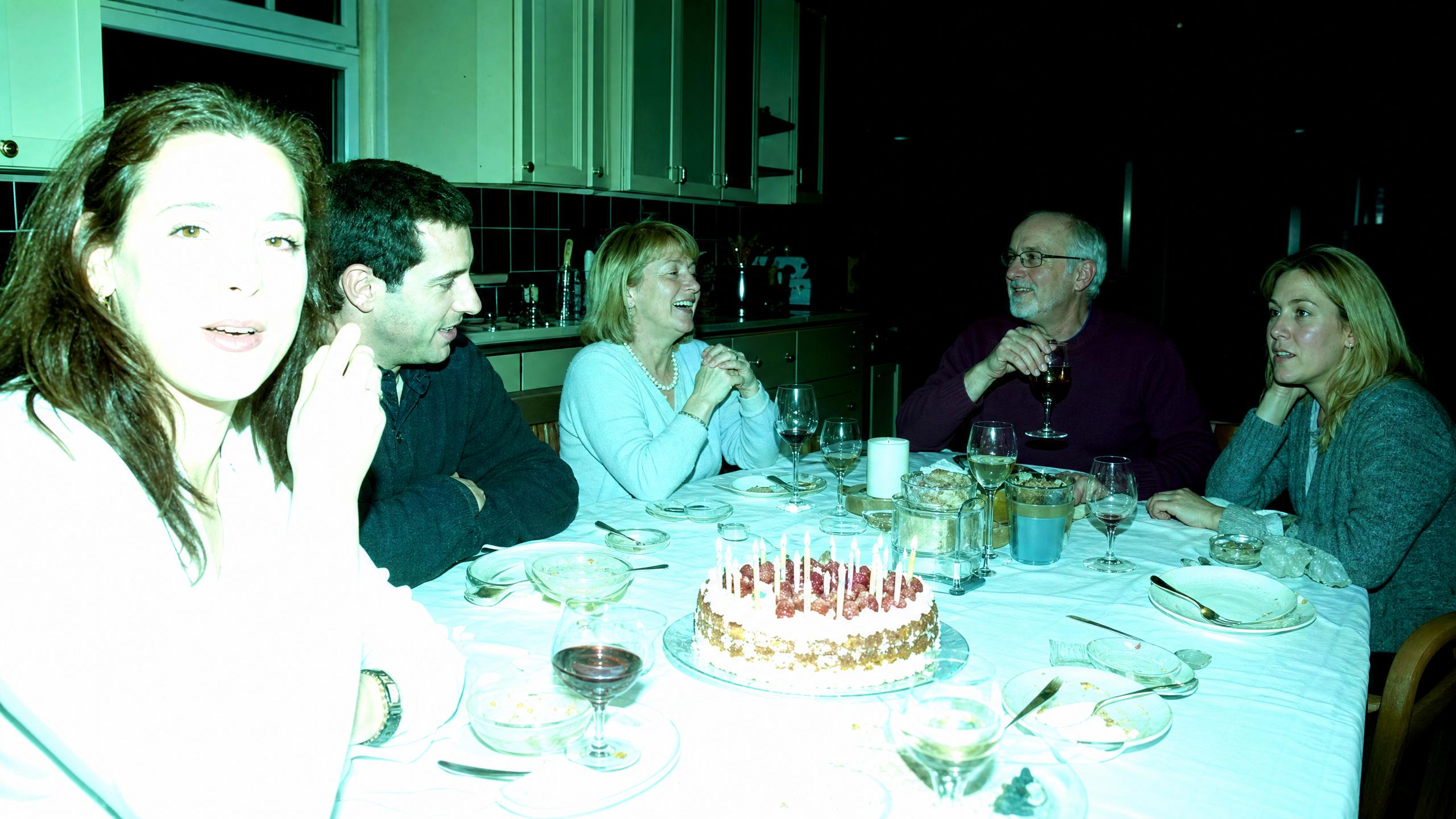 Faded snapshot with a heavy green color cast of five people at a dinner table with a birthday cake